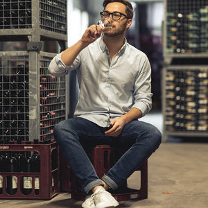 Oliver Heinrich sitzt auf einer Weinkiste und trinkt Weißwein